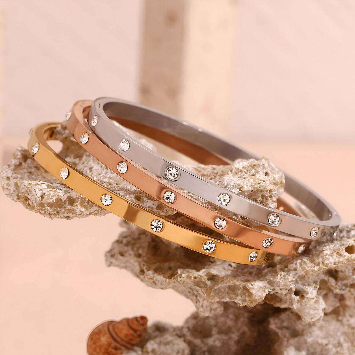 Lot de trois bracelets joncs en acier inoxydable, finitions or, or rosé et argent, ornés de petits cristaux éclatants.