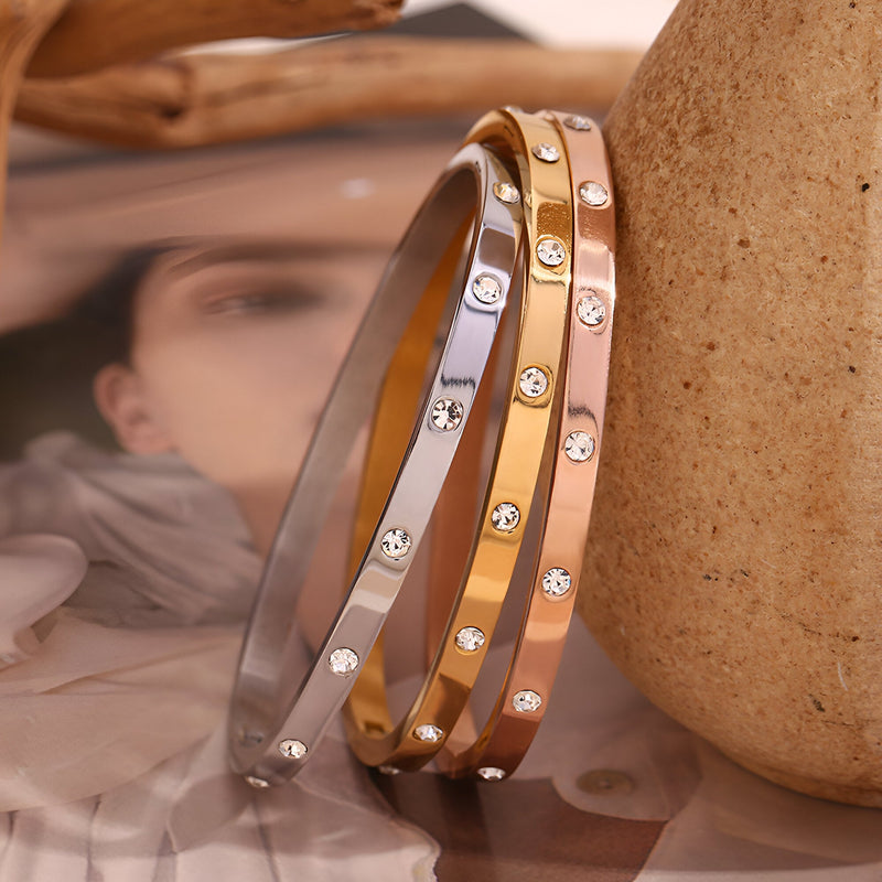 Trois bracelets joncs en acier inoxydable or, or rosé et argent avec éclats de lumière circulaires.