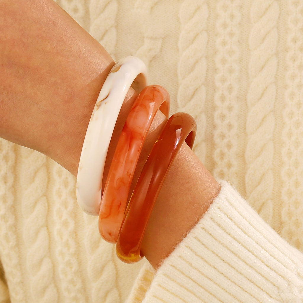 Bracelet jonc en acrylique blanc, orange translucide et marron opaque porté sur un poignet vêtu d’un pull crème côtelé.