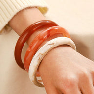 Trois bracelets joncs en acrylique, blanc marbré, orange translucide et marron, portés au poignet féminin.