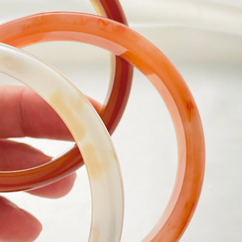 Bracelet jonc en acrylique orange translucide avec marbrures blanches et finition lisse.