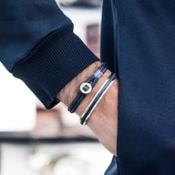 Bracelet jonc en acier inoxydable argenté avec corde bleue et fermoir rond porté sur poignet homme.