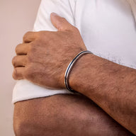 Bracelet jonc argenté en acier inoxydable avec corde noire intégrée porté au poignet masculin.