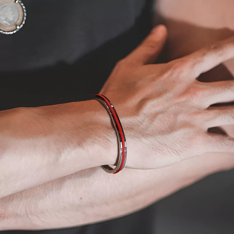 Bracelet jonc argenté avec corde rouge et noire intégrée porté au poignet masculin.