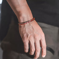 Bracelet jonc en acier inoxydable argenté avec corde rouge intégrée porté au poignet homme.