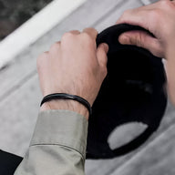 Bracelet jonc argenté avec corde noire intégrée porté sur poignet d'homme, style moderne et épuré.