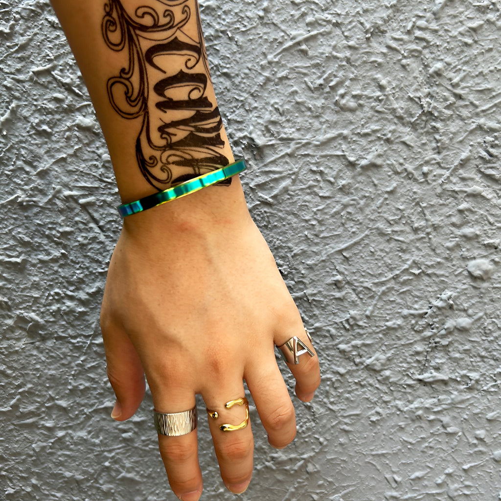 Bracelet jonc fin en acier inoxydable finition arc-en-ciel aux reflets irisés sur poignet masculin.