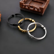 Trois bracelets joncs en acier inoxydable aux finitions argent, noir et or avec motif infini tressé.