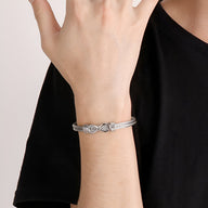 Bracelet jonc en acier inoxydable argenté avec motif infini épuré porté au poignet.