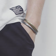 Bracelet jonc en acier inoxydable argenté avec gravures de notes de musique, style mixte, porté au poignet.