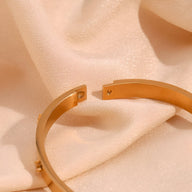 Bracelet jonc en acier inoxydable plaqué or 18 carats avec motif étoiles délicates, finition lisse et brillante.