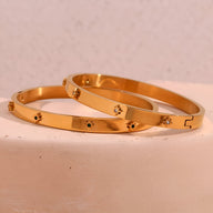 Bracelet jonc en acier doré 18 carats avec étoiles gravées et petit fermoir discret.