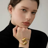 Bracelet jonc doré en acier inoxydable, design incurvé élégant portée au poignet féminin.