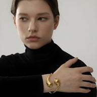 Bracelet jonc doré en acier inoxydable avec design incurvé, porté au poignet féminin.