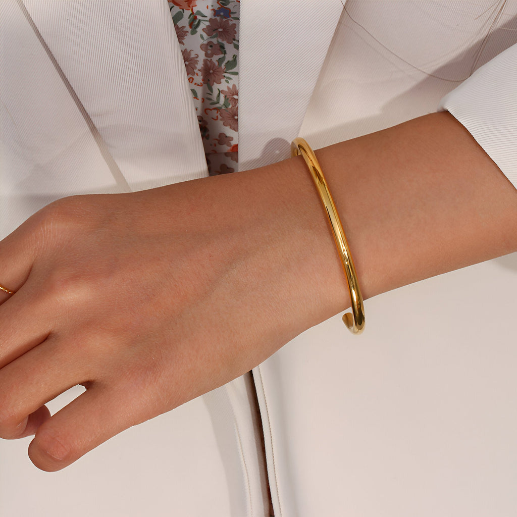 Bracelet jonc fin en acier inoxydable doré au style épuré porté au poignet.