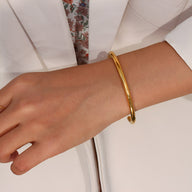 Bracelet jonc fin en acier inoxydable doré au style épuré porté au poignet.