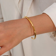Bracelet jonc en acier inoxydable doré au design épuré porté sur poignet féminin avec veste blanche.