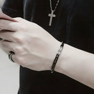 Bracelet jonc en acier inoxydable noir gravé "The Time is Now" porté au poignet homme.