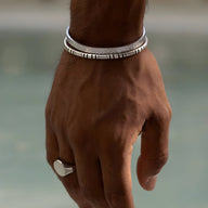 Bracelet jonc argenté en acier inoxydable fin à motifs gravés porté au poignet masculin.