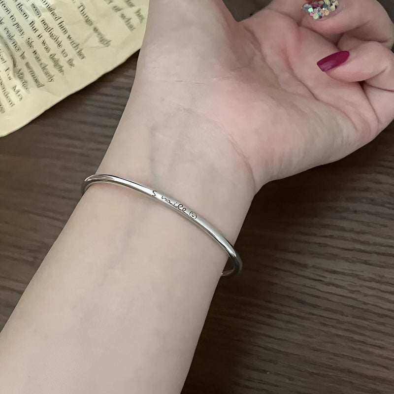 Bracelet jonc fin en argent sterling lisse, porté au poignet féminin, finition brillante.