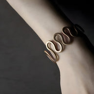 Bracelet jonc en cuivre marron à grande vague ondulée, design minimaliste et contemporain, porté au poignet.