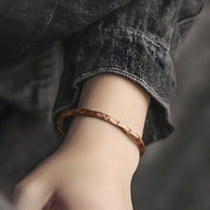 Bracelet jonc en cuivre marron au fini vieilli avec texture martelée, porté sur poignet féminin.