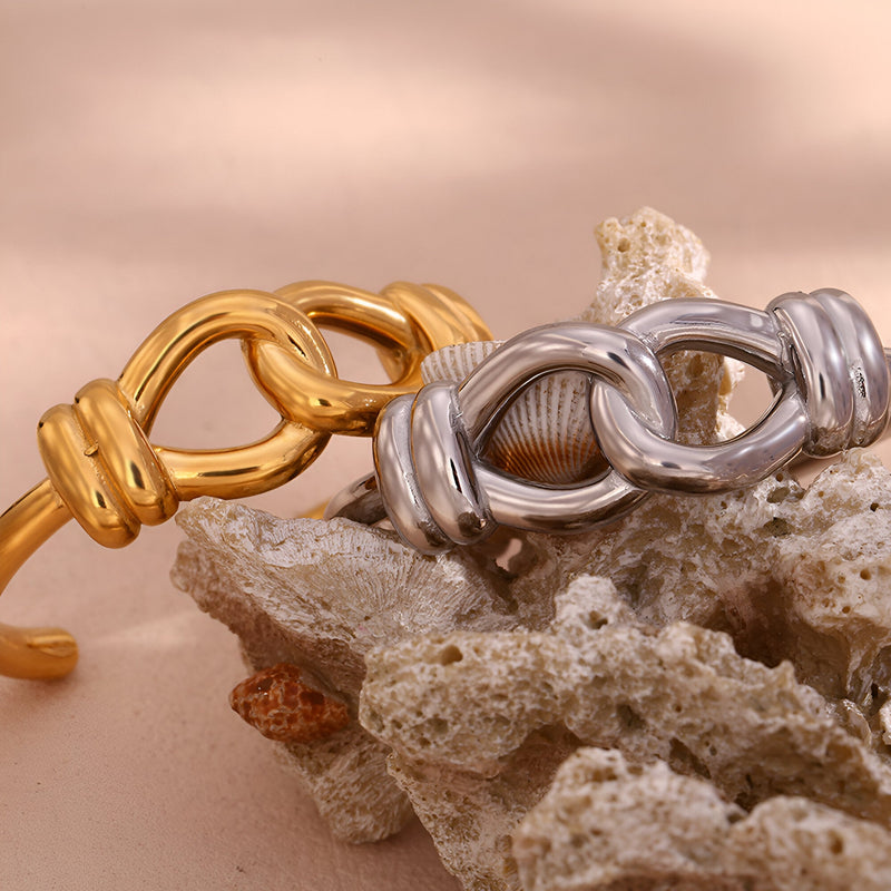 Bracelet jonc or en acier inoxydable avec design noeud d'agui et bracelet jonc argenté assorti sur roche texturée.