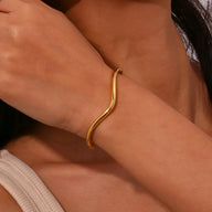 Bracelet jonc ondulé en acier inoxydable doré porté au poignet, design minimaliste et élégant.
