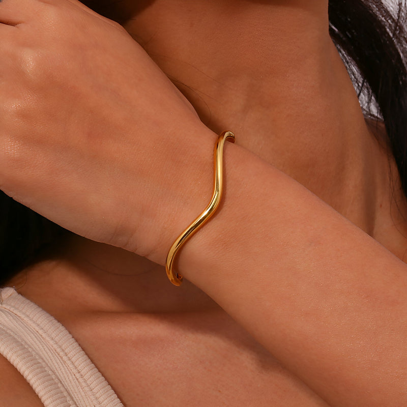 Bracelet jonc ondulé en acier inoxydable doré porté au poignet, design minimaliste et élégant.