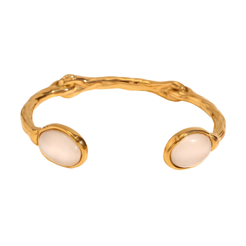 Bracelet jonc doré en acier inoxydable avec deux perles ovales rose pâle aux extrémités, finition martelée.