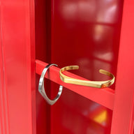 Bracelet jonc en titane doré et argenté, design épuré et minimaliste pour homme, modèle Morin posé sur surface rouge.