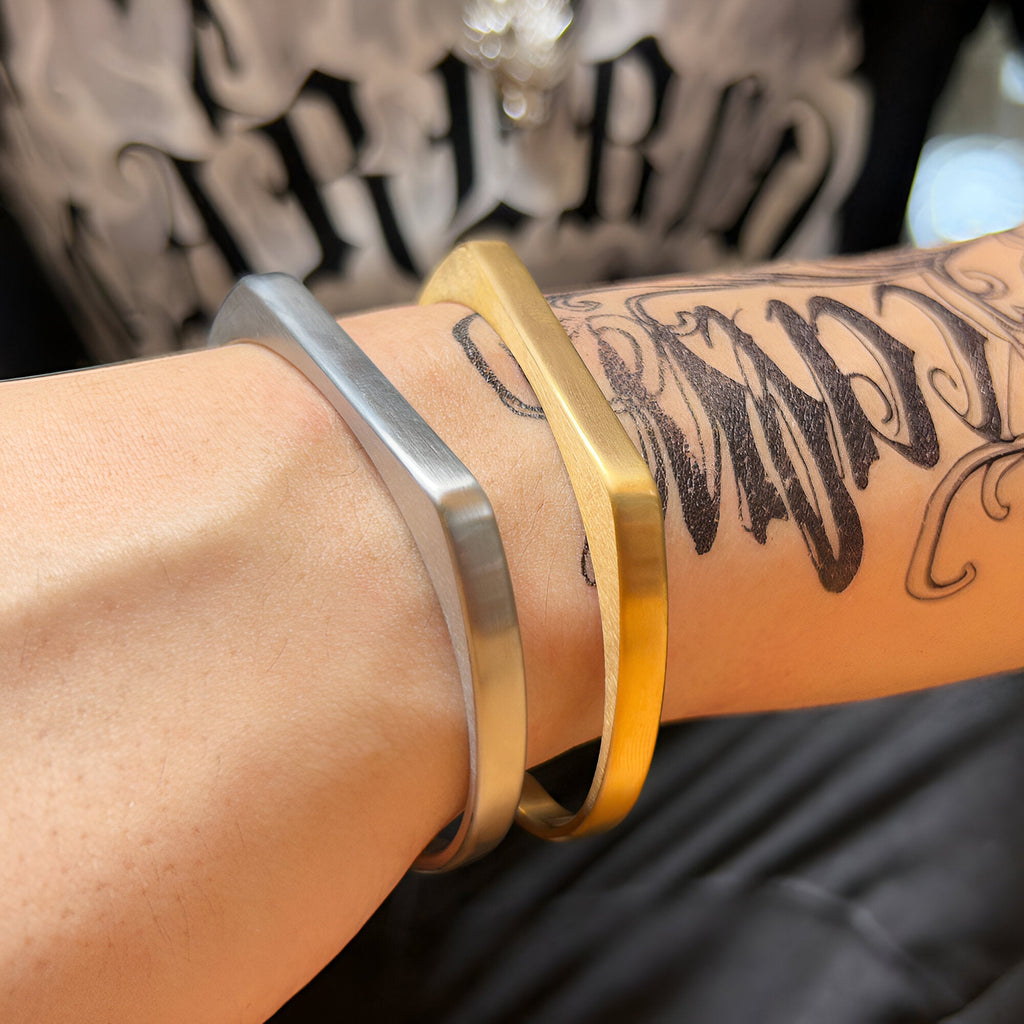 Bracelet jonc en titane argent mat et or brossé, design épuré, modèle Morin pour homme sur poignet tatoué.