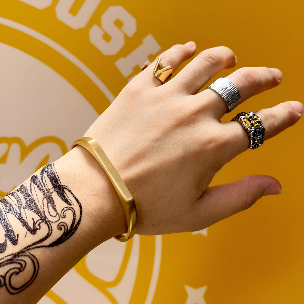 Bracelet jonc en titane or, design minimaliste, porté au poignet masculin tatoué.