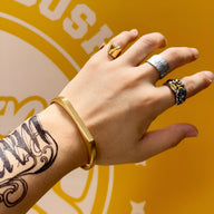 Bracelet jonc en titane or, design minimaliste, porté au poignet masculin tatoué.