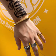 Bracelet jonc épuré en titane doré porté au poignet masculin avec trois bagues métalliques variées.