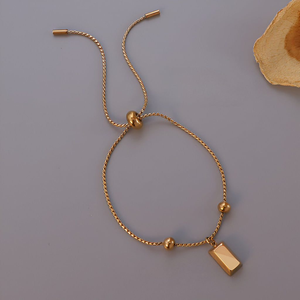 Bracelet jonc fin doré réglable avec pendentif rectangle lisse et perles rondes.