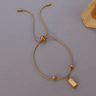 Bracelet jonc fin doré réglable avec pendentif rectangle lisse et perles rondes.