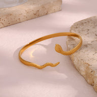 Bracelet jonc ouvert or en acier inoxydable avec motifs serpent texturés sur les extrémités.