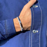 Bracelet jonc en acier inoxydable argenté avec cordon noir porté sur un poignet masculin, style minimaliste.