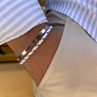 Bracelet jonc en acier inoxydable argenté avec cordon blanc à motifs noirs, porté sur poignet masculin.