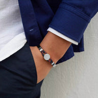 Bracelet jonc argent avec cordon bleu marine et médaillon rond porté au poignet.