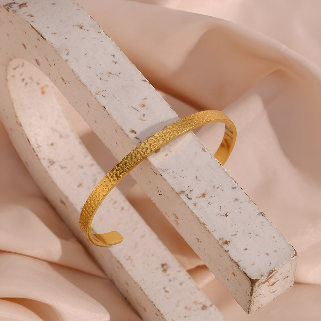 Bracelet jonc fin en acier inoxydable doré avec finition martelée élégante.