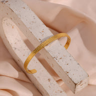 Bracelet jonc fin en acier inoxydable doré avec finition martelée élégante.