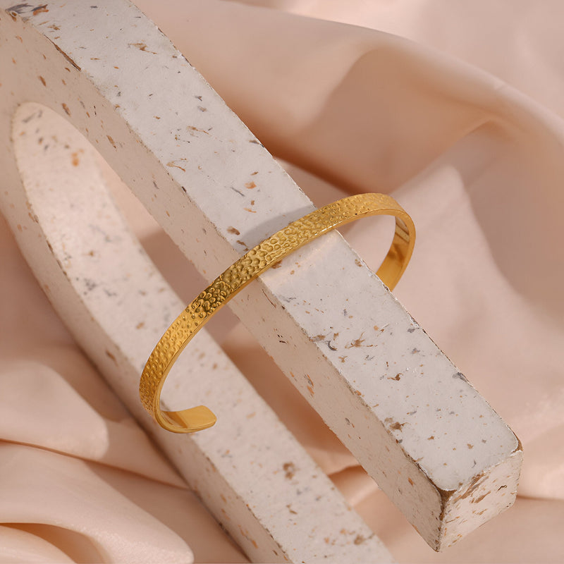 Bracelet jonc fin en acier inoxydable doré avec finition martelée élégante.