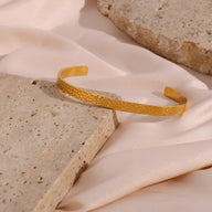 Bracelet jonc en acier inoxydable doré avec finition martelée, design épuré et élégant.