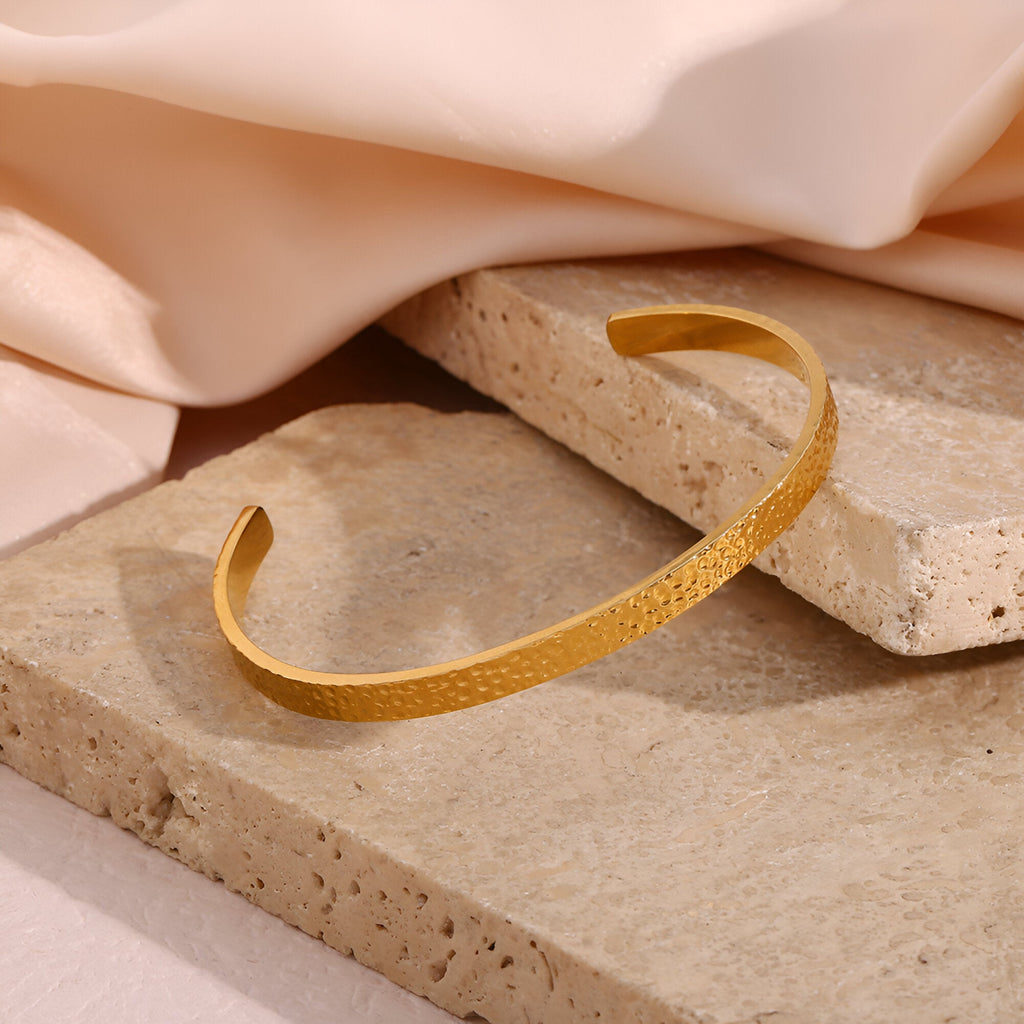 Bracelet jonc fin en acier inoxydable doré avec finition martelée texturée élégante.