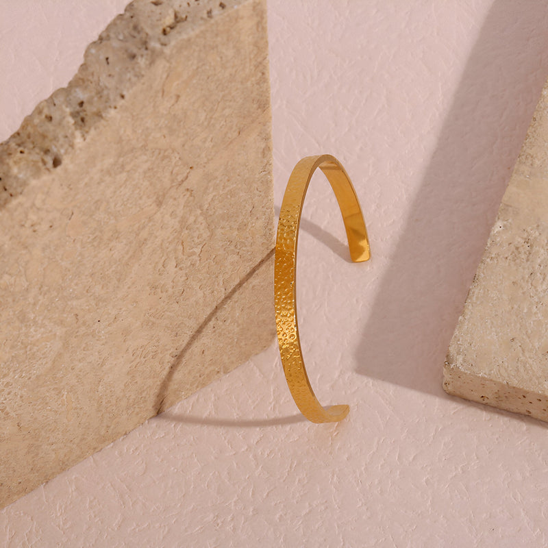 Bracelet jonc fin doré à la finition martelée en acier inoxydable, style épuré et brillant.