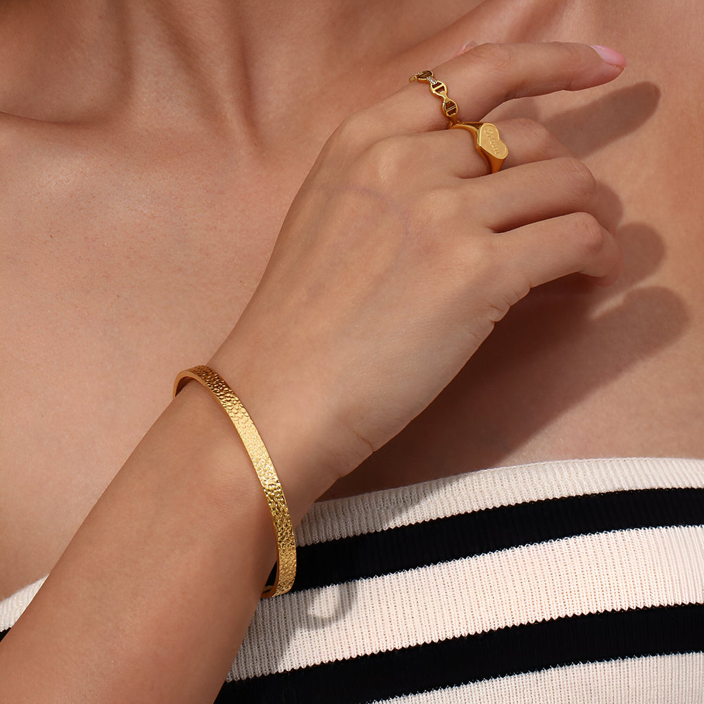 Bracelet jonc fin en acier inoxydable doré, finition martelée, porté au poignet féminin.