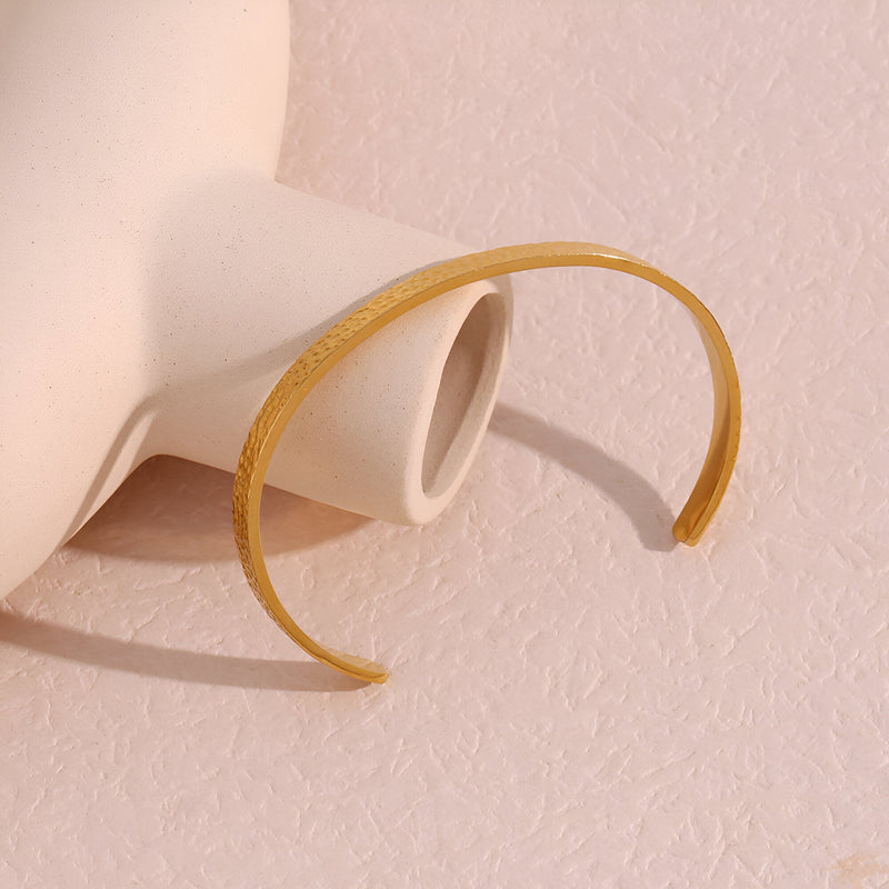 Bracelet jonc fin doré à la finition martelée en acier inoxydable, design élégant pour femme.