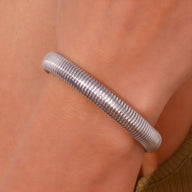 Bracelet jonc flexible en maille d'acier inoxydable argenté élégant porté au poignet.